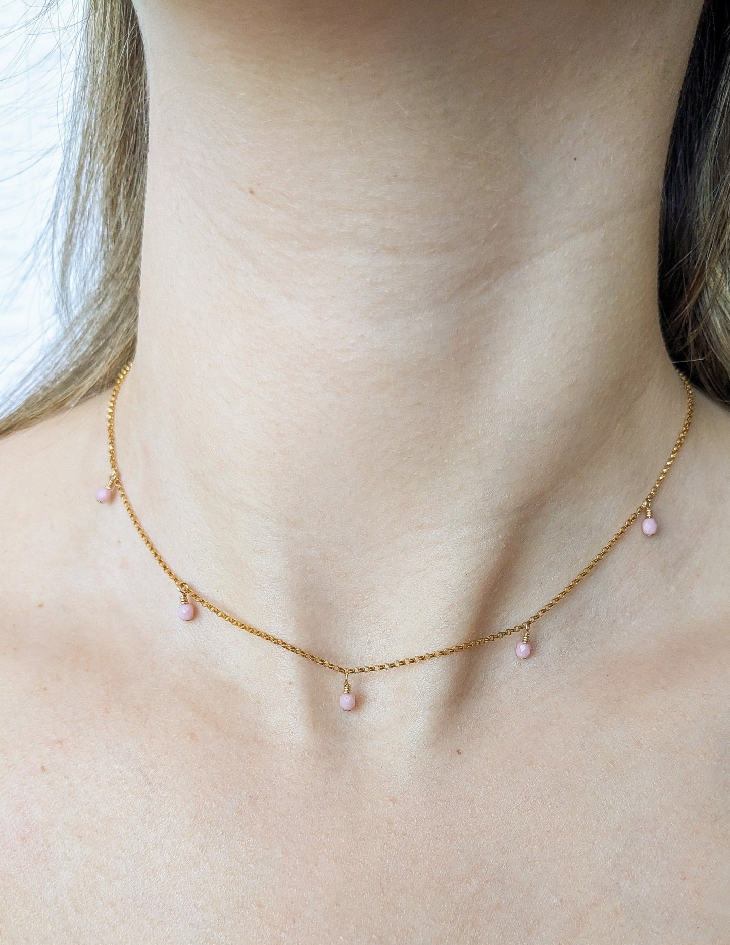 Collier Rosie porté au cou, avec petites perles roses suspendues à une fine chaîne dorée.