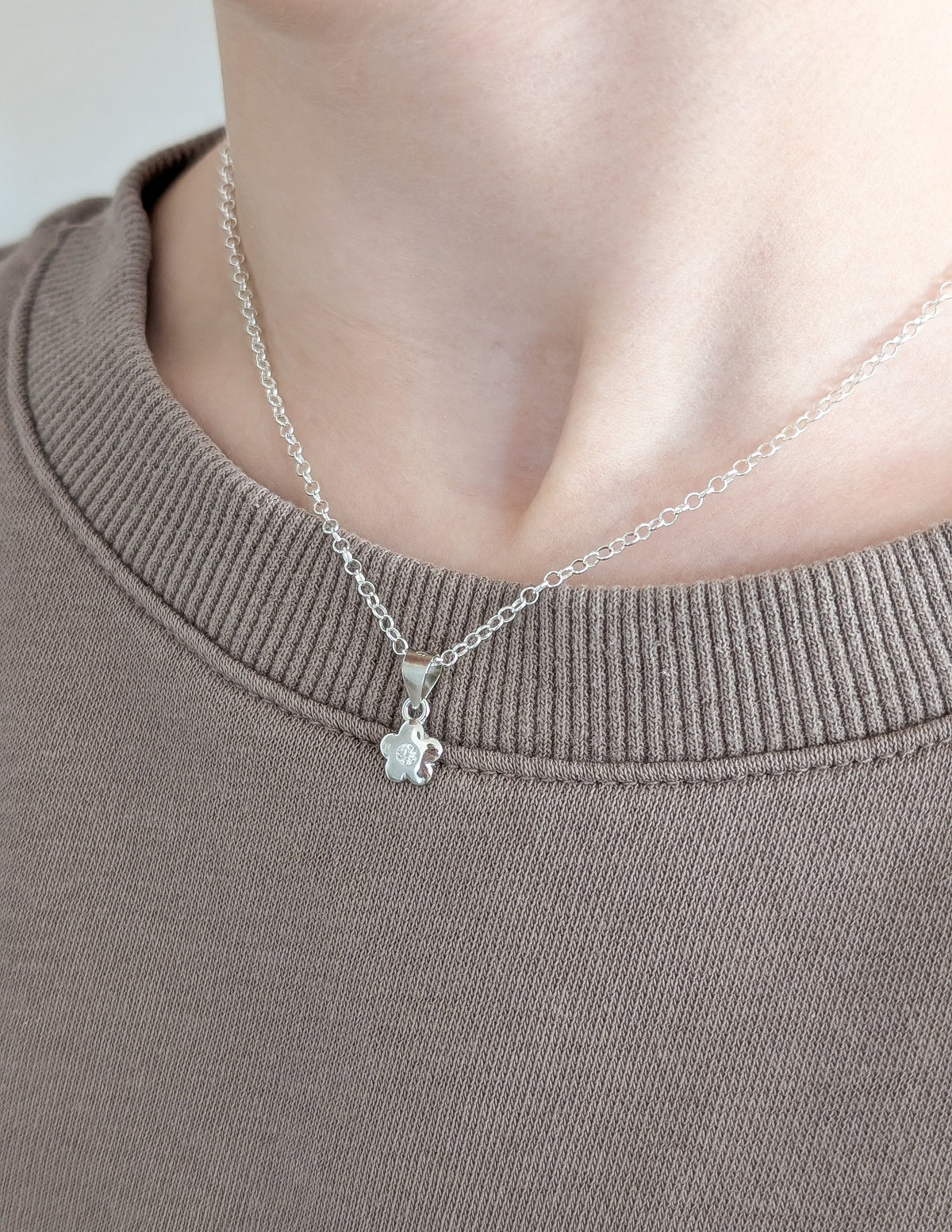 Collier Flora pour enfant porté au cou, avec sa chaîne argentée et sa petite fleur brillante.