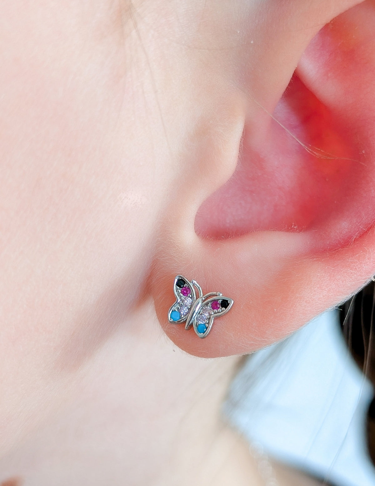 Boucle d’oreille Papillon pour enfant, en argent sterling 925 et zircons colorés, portée au lobe.