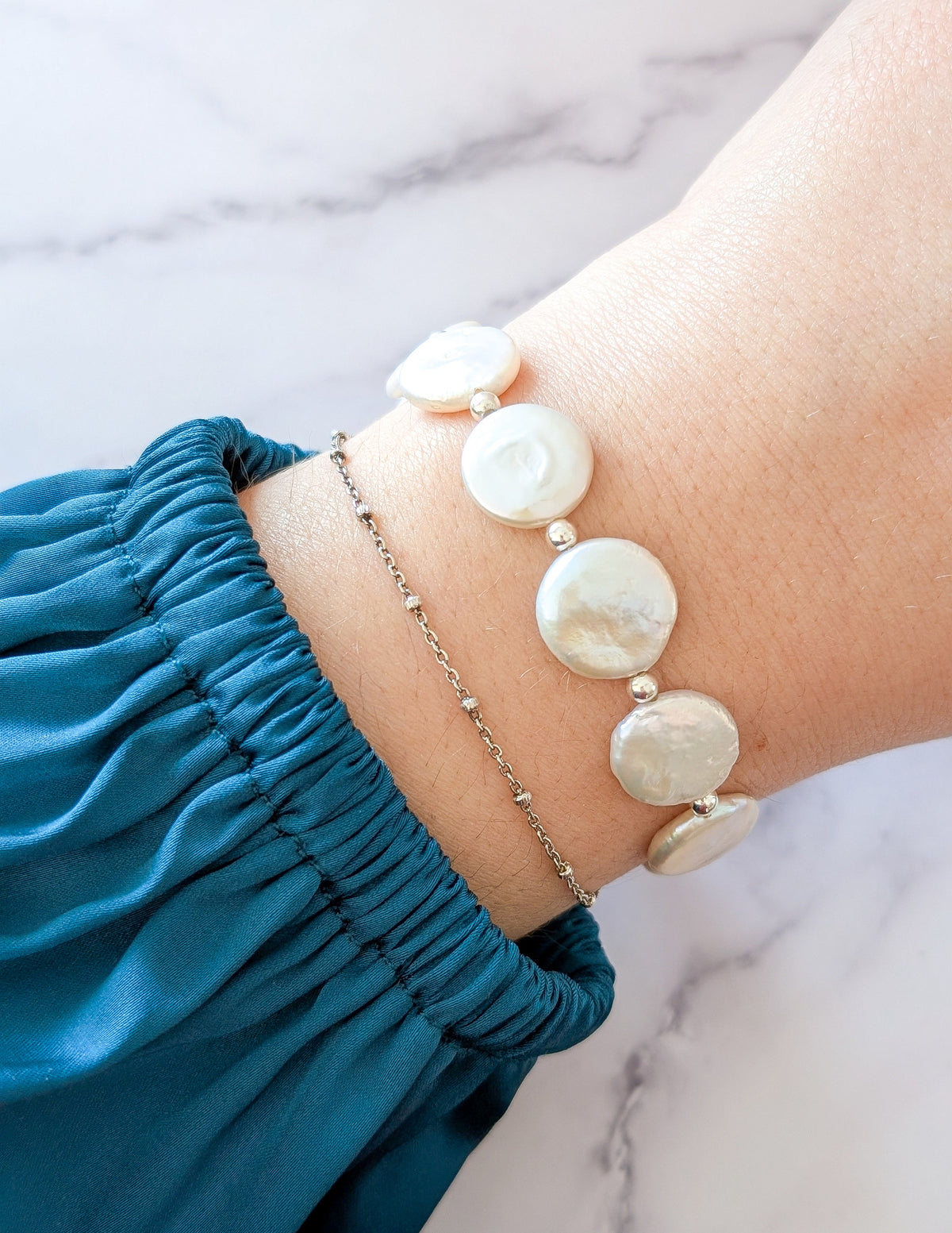 Bracelet Irisé en perles d’eau douce iridescentes porté au poignet avec un bracelet fin.