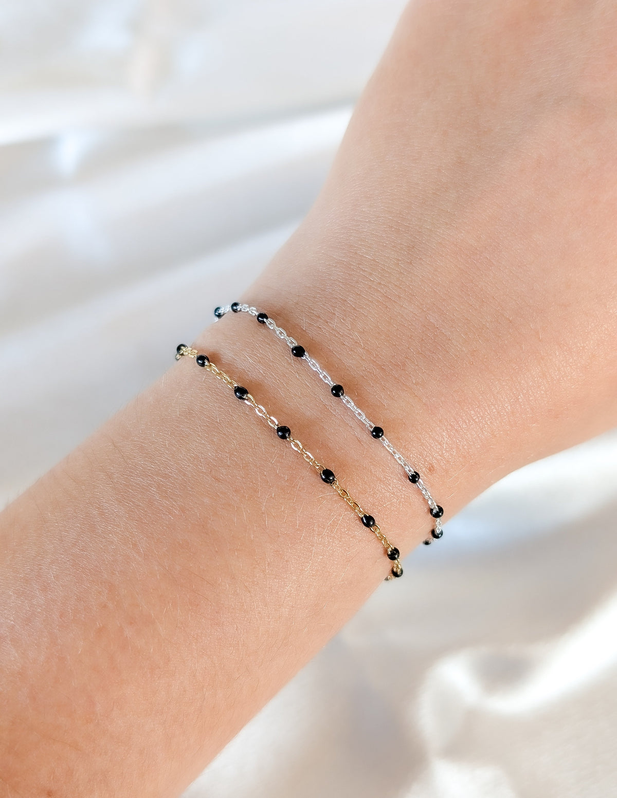 Bracelet à chaîne délicate et perles d’émail noir porté en superposition au poignet