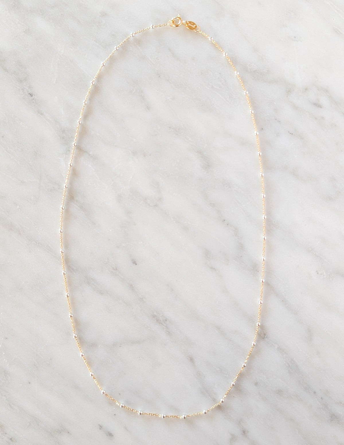 Collier Duo en gold filled 14k et argent sterling 925 présenté sur fond de marbre blanc